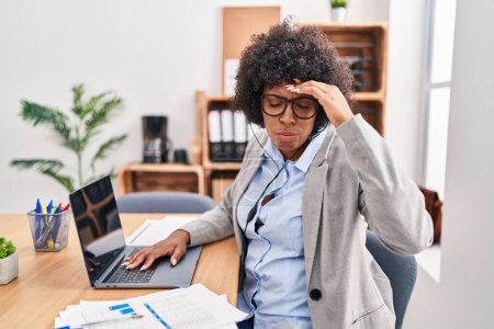 Foto de Black woman with curly hair wearing call center agent headset at the office worried and stressed about a problem with hand on forehead, nervous and anxious for crisis - Imagen libre de derechos
