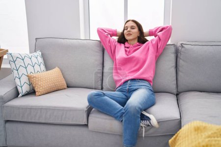 Téléchargez les photos : Young woman relaxed with hands on head sitting on sofa at home - en image libre de droit