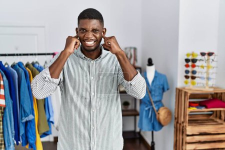 Photo for Young african american man working as manager at retail boutique covering ears with fingers with annoyed expression for the noise of loud music. deaf concept. - Royalty Free Image
