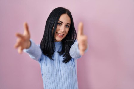Photo for Hispanic woman standing over pink background looking at the camera smiling with open arms for hug. cheerful expression embracing happiness. - Royalty Free Image
