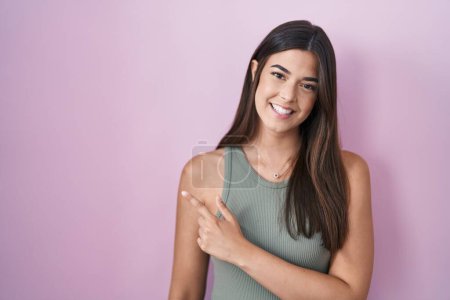 Téléchargez les photos : Femme hispanique debout sur fond rose gai avec un sourire du visage pointant avec la main et le doigt sur le côté avec une expression heureuse et naturelle sur le visage - en image libre de droit