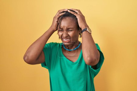 Photo for African woman with dreadlocks standing over yellow background suffering from headache desperate and stressed because pain and migraine. hands on head. - Royalty Free Image