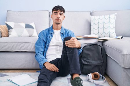 Photo for Young hispanic man sitting on the floor studying for university relaxed with serious expression on face. simple and natural looking at the camera. - Royalty Free Image