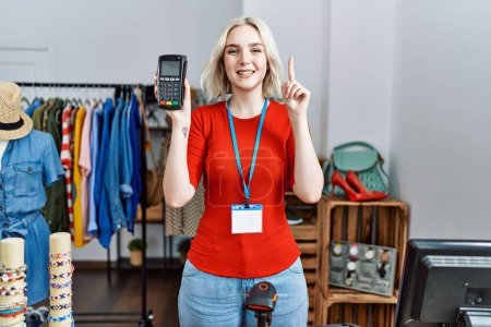 Photo for Young caucasian woman working as manager at retail boutique holding dataphone smiling with an idea or question pointing finger with happy face, number one - Royalty Free Image