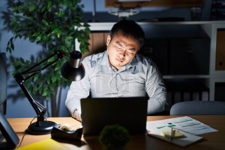 Photo for Young chinese man working using computer laptop at night with hand on stomach because nausea, painful disease feeling unwell. ache concept. - Royalty Free Image