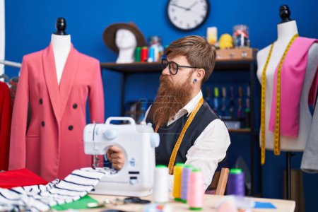 Téléchargez les photos : Jeune tailleur rousse homme utilisant une machine à coudre à l'usine de vêtements - en image libre de droit