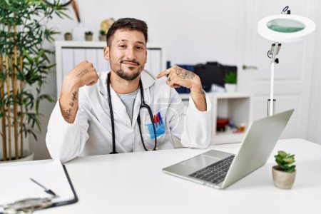 Photo for Young doctor working at the clinic using computer laptop looking confident with smile on face, pointing oneself with fingers proud and happy. - Royalty Free Image