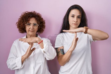 Hispanic mother and daughter wearing casual white t shirt over pink background doing time out gesture with hands, frustrated and serious face  tote bag #621065746