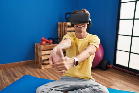 Téléchargez les photos : Jeune homme caucasien utilisant des lunettes de réalité virtuelle étirant au centre sportif - en image libre de droit