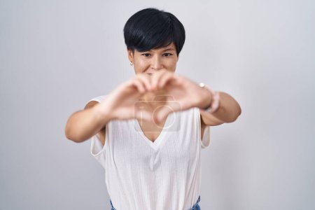 Foto de Young asian woman with short hair standing over isolated background smiling in love doing heart symbol shape with hands. romantic concept. - Imagen libre de derechos