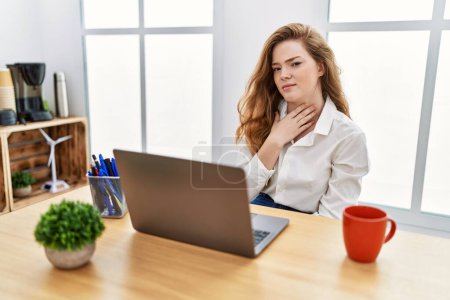 Téléchargez les photos : Jeune femme caucasienne travaillant au bureau à l'aide d'un ordinateur portable touchant le cou douloureux, mal de gorge pour la grippe, la motte et l'infection - en image libre de droit