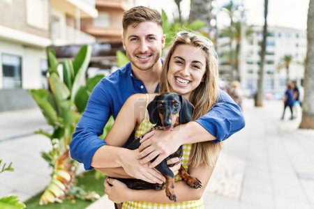 Téléchargez les photos : Jeune couple caucasien souriant heureux et câlin avec chien sur la promenade. - en image libre de droit