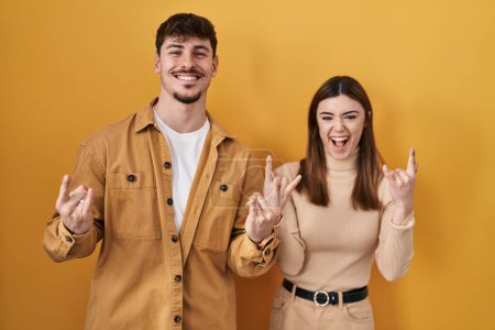 Photo for Young hispanic couple standing over yellow background shouting with crazy expression doing rock symbol with hands up. music star. heavy music concept. - Royalty Free Image