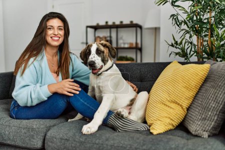 Photo for Young woman hugging dog sitting on sofa at home - Royalty Free Image