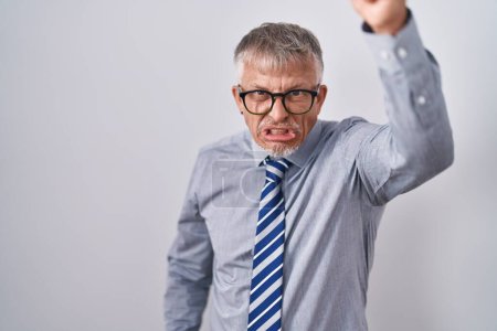 Téléchargez les photos : Homme d'affaires hispanique aux cheveux gris portant des lunettes en colère et fou levant le poing frustré et furieux tout en criant de colère. rage et concept agressif. - en image libre de droit