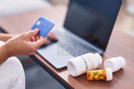 Foto de Young blonde woman using laptop and credit card buying pills at home - Imagen libre de derechos
