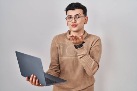 Foto de Non binary person using computer laptop looking at the camera blowing a kiss with hand on air being lovely and sexy. love expression. - Imagen libre de derechos