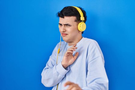 Téléchargez les photos : Non binary person listening to music using headphones disgusted expression, displeased and fearful doing disgust face because aversion reaction. - en image libre de droit