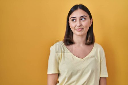 Foto de Hispanic girl wearing casual t shirt over yellow background smiling looking to the side and staring away thinking. - Imagen libre de derechos