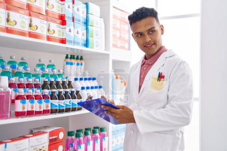 Téléchargez les photos : Young latin man pharmacist smiling confident writing report at pharmacy - en image libre de droit
