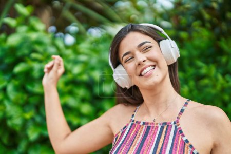 Photo for Young beautiful hispanic woman listening to music and dancing at park - Royalty Free Image
