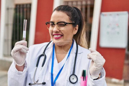 Photo for Young hispanic doctor woman doing coronavirus infection nasal test winking looking at the camera with sexy expression, cheerful and happy face. - Royalty Free Image