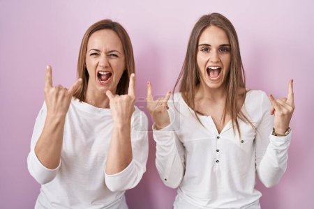 Téléchargez les photos : Middle age mother and young daughter standing over pink background shouting with crazy expression doing rock symbol with hands up. music star. heavy music concept. - en image libre de droit
