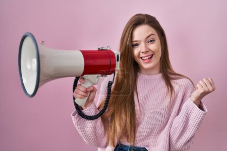 Photo for Young caucasian woman shouting through megaphone screaming proud, celebrating victory and success very excited with raised arm - Royalty Free Image