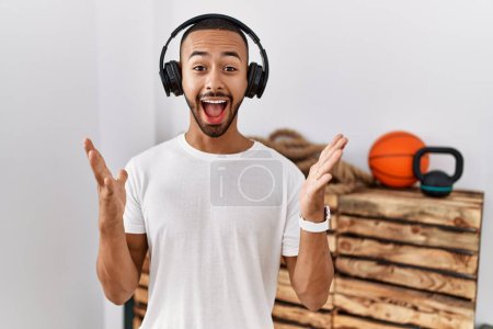 Foto de African american man listening to music using headphones at the gym celebrating crazy and amazed for success with arms raised and open eyes screaming excited. winner concept - Imagen libre de derechos
