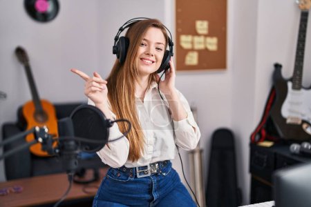 Photo for Young caucasian woman recording song at music studio smiling happy pointing with hand and finger to the side - Royalty Free Image