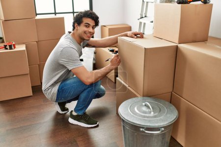 Téléchargez les photos : Jeune homme hispanique souriant heureux boîtes d'emballage à la nouvelle maison. - en image libre de droit