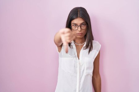 Photo for Brunette young woman standing over pink background wearing glasses looking unhappy and angry showing rejection and negative with thumbs down gesture. bad expression. - Royalty Free Image