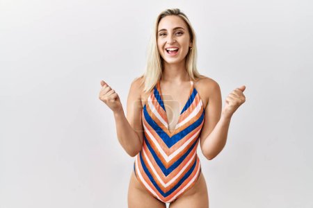 Photo for Young blonde woman wearing swimsuit over isolated background celebrating surprised and amazed for success with arms raised and open eyes. winner concept. - Royalty Free Image