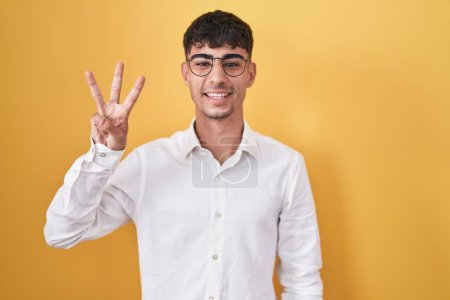 Photo for Young hispanic man standing over yellow background showing and pointing up with fingers number three while smiling confident and happy. - Royalty Free Image