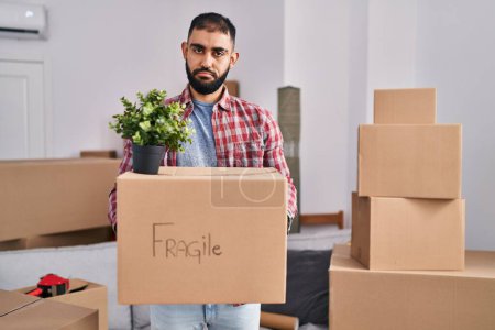 Photo for Middle east man with beard moving to a new home holding cardboard box depressed and worry for distress, crying angry and afraid. sad expression. - Royalty Free Image