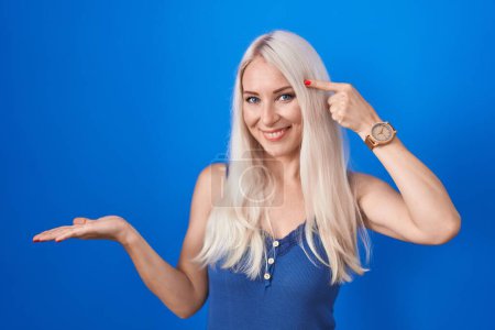Photo for Caucasian woman standing over blue background confused and annoyed with open palm showing copy space and pointing finger to forehead. think about it. - Royalty Free Image