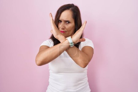 Téléchargez les photos : Moyen âge brunette femme debout sur fond rose expression de rejet croisement bras faisant signe négatif, visage en colère - en image libre de droit