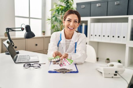 Foto de Joven morena médico mujer sosteniendo pastillas sonriendo y riendo en voz alta porque broma loca divertida. - Imagen libre de derechos