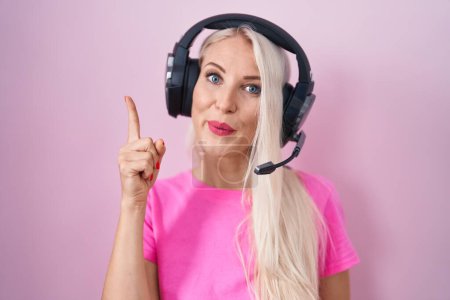 Téléchargez les photos : Caucasian woman listening to music using headphones pointing finger up with successful idea. exited and happy. number one. - en image libre de droit