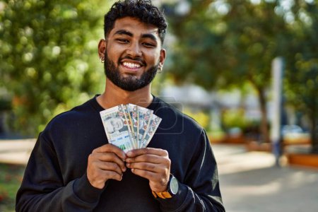 Téléchargez les photos : Jeune homme arabe souriant confiant tenant sol billets péruviens au parc - en image libre de droit