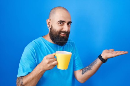Téléchargez les photos : Young hispanic man with beard and tattoos drinking a cup of coffee pointing aside with hands open palms showing copy space, presenting advertisement smiling excited happy - en image libre de droit