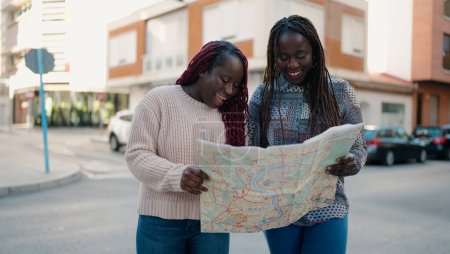 Foto de Dos amigos afroamericanos sonriendo confiados buscando mapa de la ciudad en la calle - Imagen libre de derechos