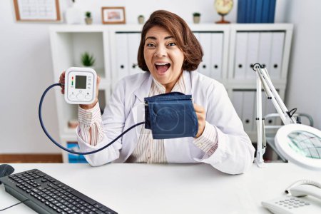 Photo for Middle age hispanic doctor woman using blood pressure monitor celebrating crazy and amazed for success with open eyes screaming excited. - Royalty Free Image