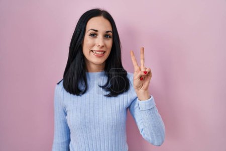 Téléchargez les photos : Femme hispanique debout sur fond rose montrant et pointant vers le haut avec les doigts numéro deux tout en souriant confiant et heureux. - en image libre de droit