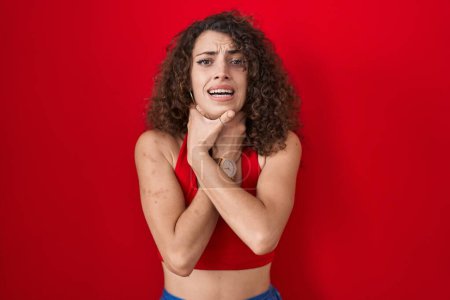Téléchargez les photos : Hispanic woman with curly hair standing over red background shouting suffocate because painful strangle. health problem. asphyxiate and suicide concept. - en image libre de droit