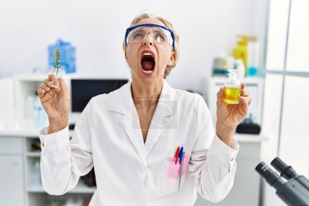 Photo for Middle age blonde woman working at laboratory angry and mad screaming frustrated and furious, shouting with anger looking up. - Royalty Free Image