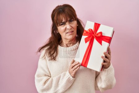 Photo for Middle age hispanic woman holding present clueless and confused expression. doubt concept. - Royalty Free Image