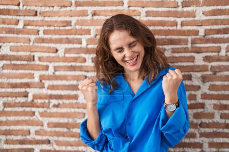 Photo for Beautiful brunette woman standing over bricks wall very happy and excited doing winner gesture with arms raised, smiling and screaming for success. celebration concept. - Royalty Free Image