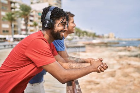 Téléchargez les photos : Deux Afro-Américains souriant heureux d'écouter de la musique à la plage. - en image libre de droit