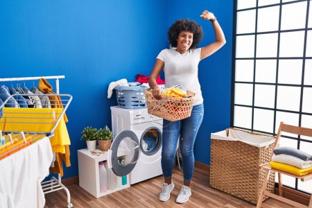 Photo for African american woman smiling confident holding basket with clothes at laundry room - Royalty Free Image